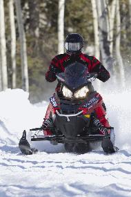 Man rides a red snowmobile over snow.
